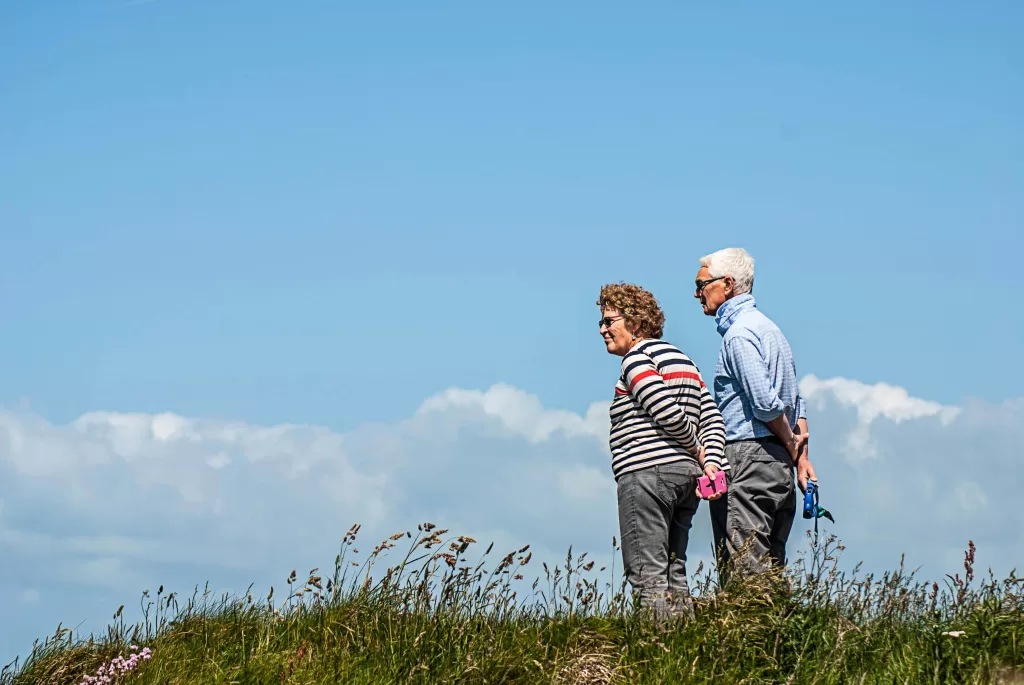a man and woman standing outside in green grass with a blue sky behind them